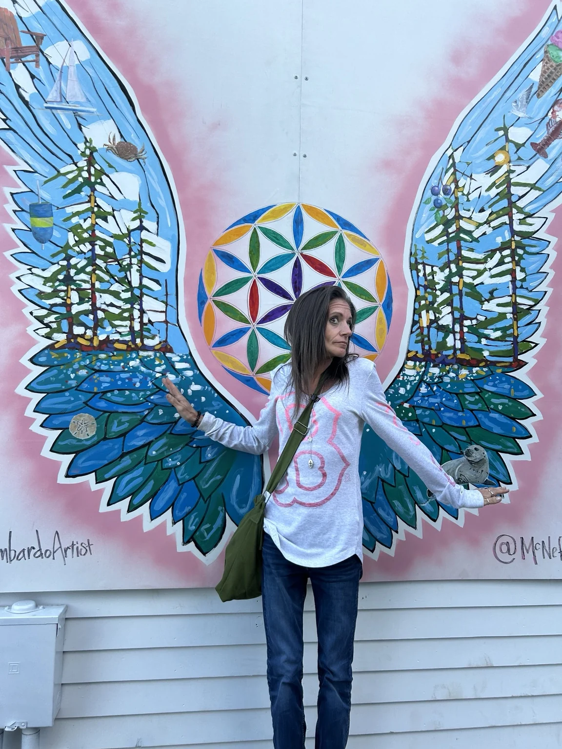 Katie standing before a colorful mural painted as wings